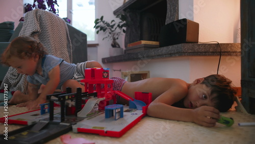Quadro em tela Toddler crawling on floor near toy garage set while older brother rests beside h