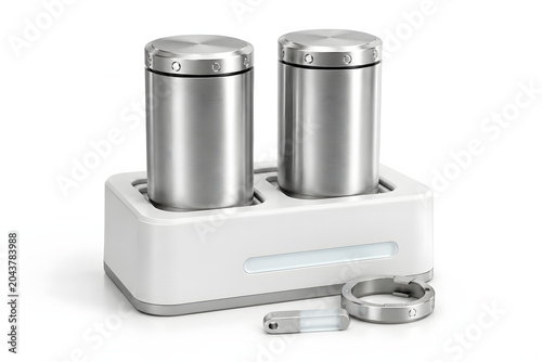 Two modern stainless steel battery cylinders rest in a minimalist white charging dock, accompanied by a small battery and a metal ring.