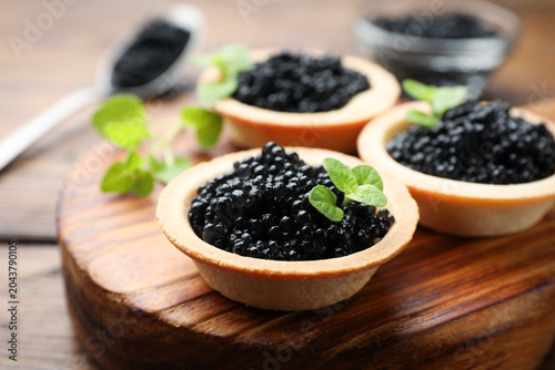 Canvastavla Tasty tartlets with black caviar on wooden table, closeup