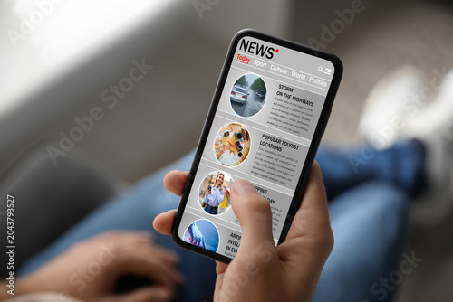 фотографія Man reading online newspaper on mobile phone indoors, closeup