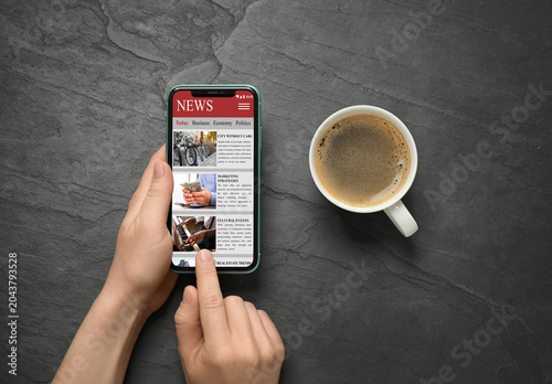 фотографія Woman reading online newspaper on mobile phone at grey textured background, top