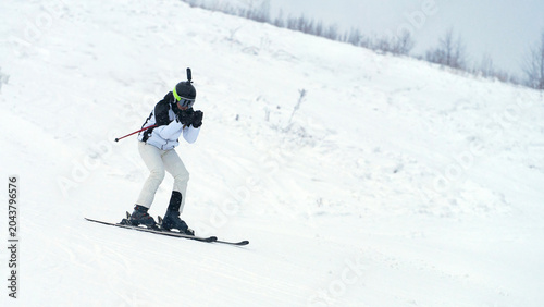A lone female skier skis down a snowy slope. She has a webcam mounted on her helmet.