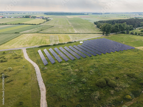 Aerial high angle view of a solar farm with rows of photovoltaic panels in a rural field landscape surrounded by trees in Poland