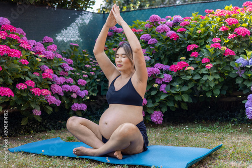 Pregnant woman finding peace and balance, meditating in a lotus pose on a yoga mat outdoors, surrounded by vibrant hydrangea flowers, embracing wellness during pregnancy