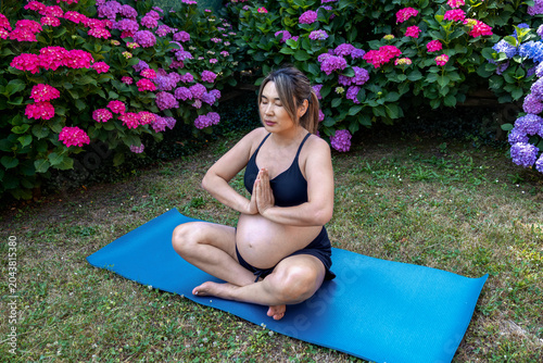 Pregnant woman practicing prenatal yoga in a lotus position, finding tranquility and balance amidst a vibrant garden, promoting health and wellness during pregnancy
