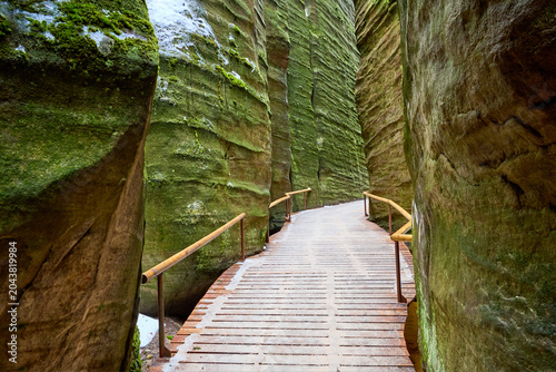 Foto Narrow wooden pathway through moss-covered rock formations in a serene gorge