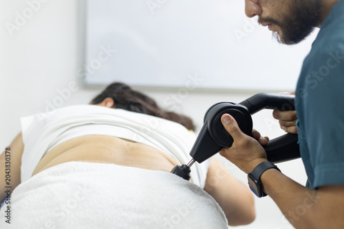 Принти на полотні Close-up view of a physiotherapist using a percussion massage device on a patient's lower back during a physical therapy session