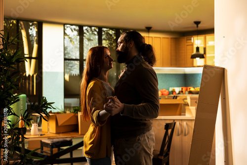 Valokuva Young partners hugging and dancing among cardboard boxes in their new house indoors, Romantic moment capturing the happiness and satisfaction of homeowners celebrating fresh start