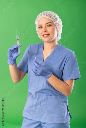 Obraz na plátně Smiling young woman medic in blue uniform holding syringe ready to apply