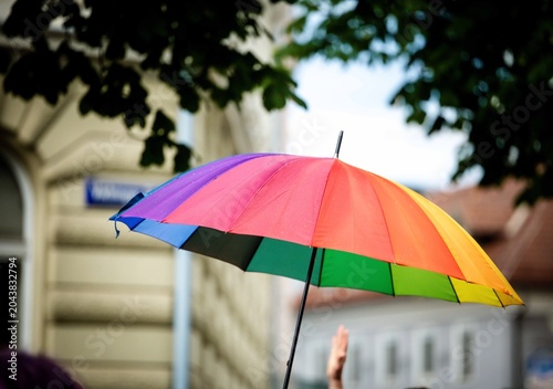 Colorful rainbow umbrella in urban setting with green foliage and classic architecture during pride parade in Klagenfurt Austria