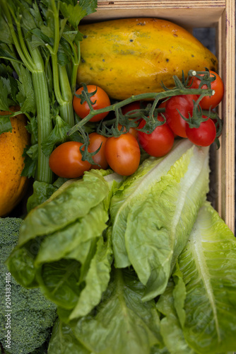 Romaine lettuce and cherry tomatoes are filling wooden crate on market stall, colorful textures