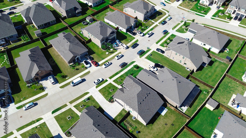 Curved street enclave in Arlington, TX presents rows of homes with gray brown roofs, fenced backyards parked cars arranged along gently bending roads. Surrounding tree lines distant commercial