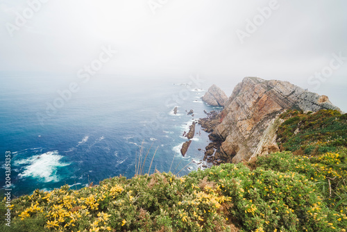 Tableau sur toile Rugged cliffs at Cabo de Penas drop into the deep blue Atlantic, framed by yello