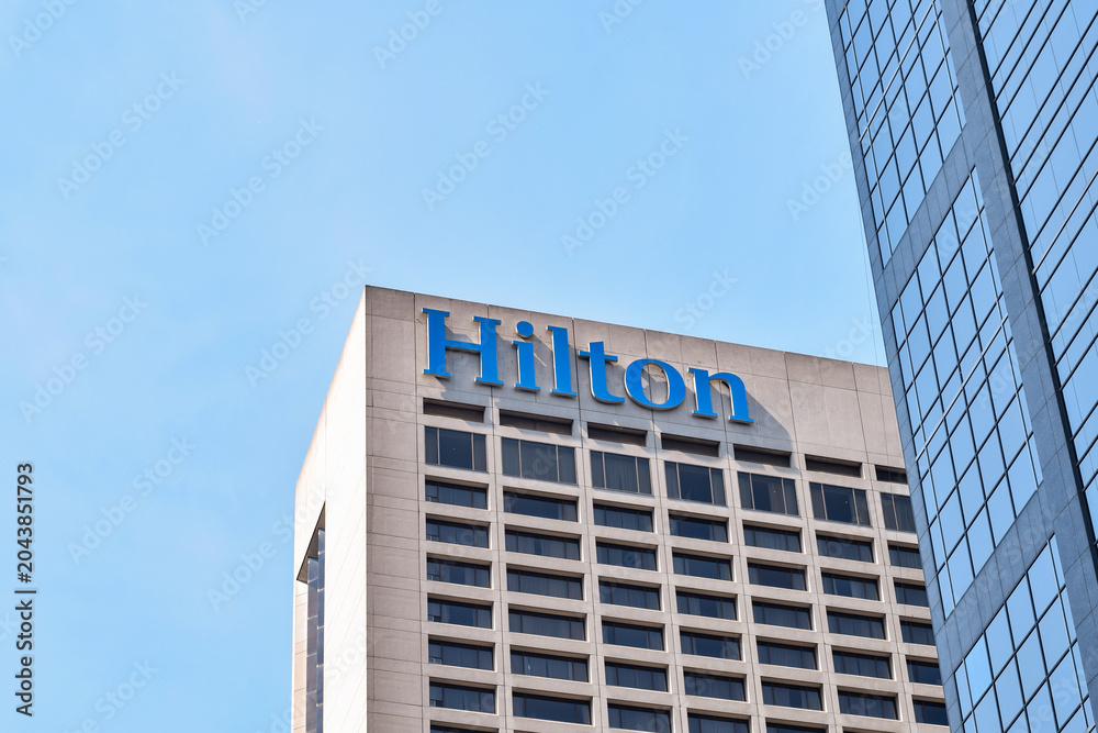 Naklejka premium Minimal architectural view of the upper portion of a modern high rise building featuring a Hilton hotel sign in downtown Toronto against a clear sky, May 2026