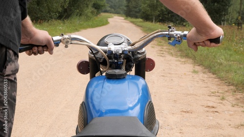 Bild auf Leinwand Rider hands gripping blue vintage motorcycle handlebars, navigating a winding di
