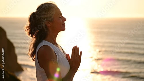 Woman meditating in yoga pose by ocean at sunset