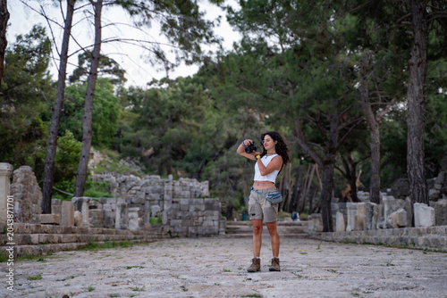 Young female photographer checking pictures on her camera at Phaselis ancient city in Turkey.