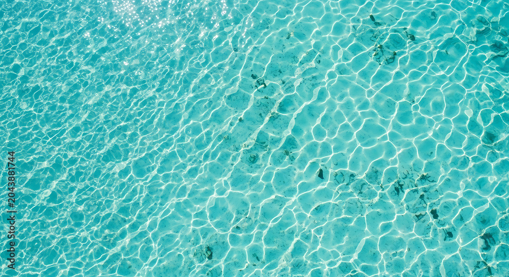 Obraz premium Crystal clear turquoise water surface with sunlight reflections and rippling waves.