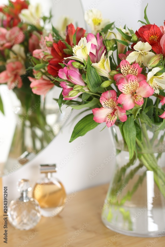 Obraz premium Bouquet of alstroemeria flowers in vase and perfumes on dressing table indoors, closeup