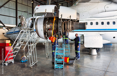 Two plane technicians working on open turboprop airplane engine during mechanical inspection and repair inside hangar.