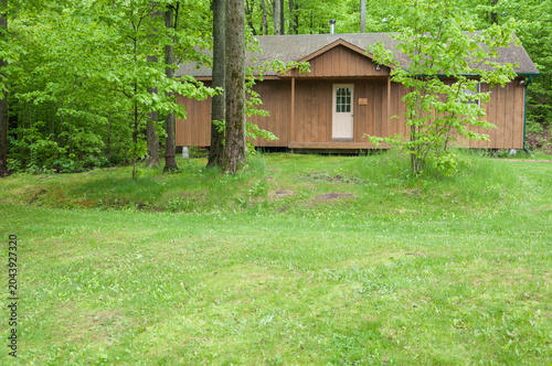 Small wooden cabin surrounded by lush green forest in a peaceful natural setting.