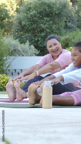 Vertical video: Stretching mom and daughter reaching toes on patio mats with watch bottle in pink
