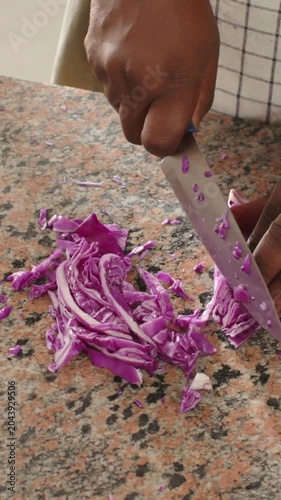 Vertical video: Gripping blue knife, cook hands cutting red cabbage on speckled counter for slaw