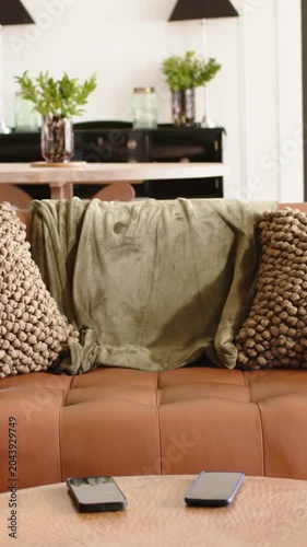 Vertical video: Shifting camera revealing brown sofa with olive throw at home showing two phones
