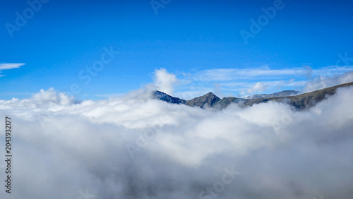 Fotografie Mountain peaks above a sea of clouds under clear blue sky