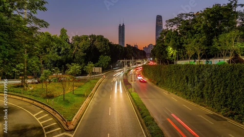 Evening Traffic on Tree-Lined City Road with Skyline at Sunset