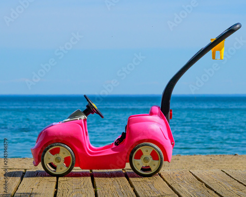 Photography Bright pink child's push car on wooden boardwalk at Kew Beach with Lake Ontario and blue sky, Toronto, Ontario