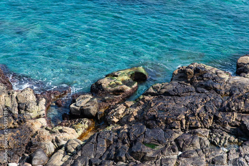 High angle view of dark coastal rocks with green moss and clear water