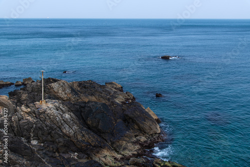 Metal pole on a dark rocky coastal cliff overlooking the sea