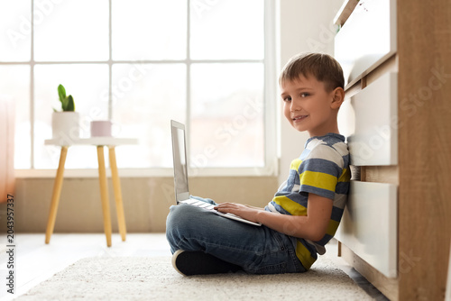 Cute little boy with modern laptop sitting on floor at home