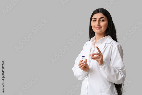 Beautiful young female doctor with syringe and ampule on white background