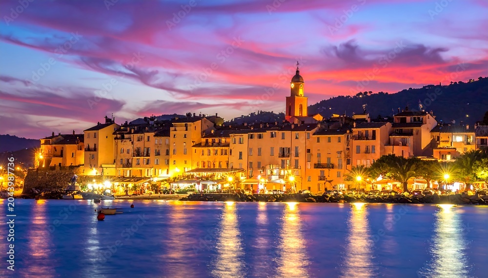 Obraz premium Coastal town buildings illuminated at twilight, reflecting on calm water, beneath vibrant pink, purple, and blue sky