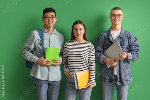 Happy students with notebooks and laptop on green background