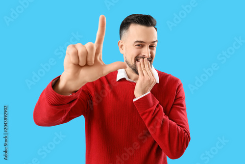Bild auf Leinwand Handsome man showing loser gesture on blue background