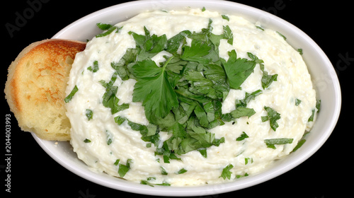 Creamy dip topped with fresh green herbs served in a bowl with a side of toasted bread, appetizer