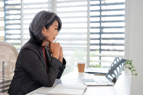  Middle aged business woman using laptop working in corporate office. Mature professional businesswoman executive at work, female manager looking at computer at desk thinking on project.