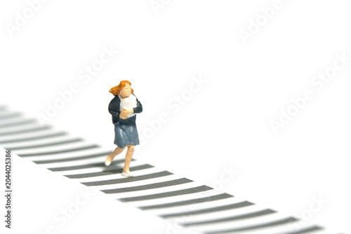 Miniature tiny people toy photography. Front view of a girl pupil student running on zebra crossing crosswalk. Isolated on a white background