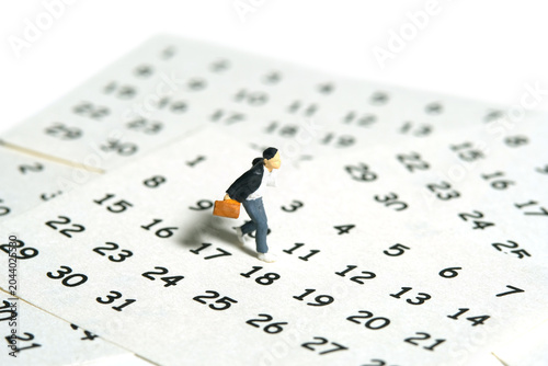 Miniature people toy figure photography. A boy pupil student running above calendar. Isolated on a white background