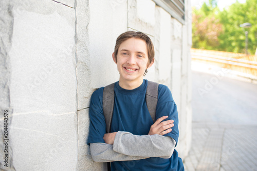 Photos Smiling teenage schoolboy student with backpack leaning against stone wall