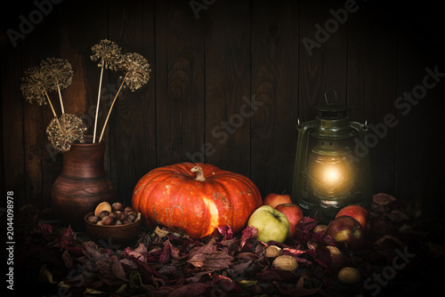 Magical autumn still life with pumpkin and old kerosene lantern among apples and dry leaves on wooden background, low key