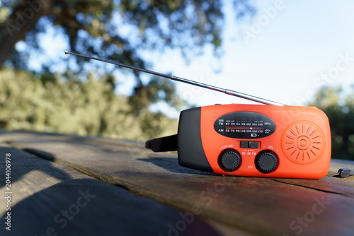 Photos Orange hand crank radio with antenna on a wooden table, receiving essential info
