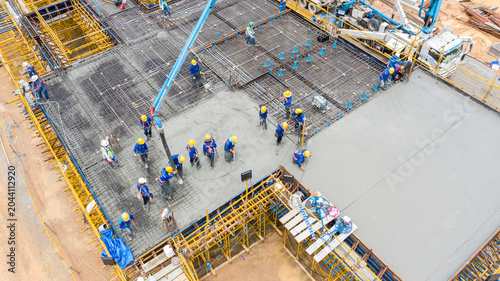 Photos Construction Site Concrete Pour: An aerial view showcases a bustling construction site where workers in hard hats are actively pouring concrete, creating a solid foundation for a new structure