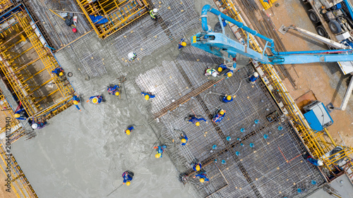 Fotografie Construction Site Aerial View: An aerial perspective of a busy construction site where workers in yellow hard hats pour concrete, showcasing industrial progress and development