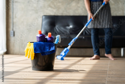 A young butler cleans the floor, mops the floor, carries a mop and a plastic bucket with brushes, gloves and detergent out of the room.