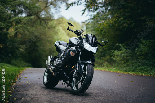 Tableau sur toile Black sports motorcycle standing on a forest road on a background of green trees