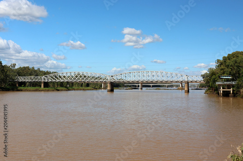 Historic steel truss spans of the heritage-listed Alexandra Railway Bridge crossing the Fitzroy River under a bright, partly cloudy sky in Rockhampton, Queensland, Australia